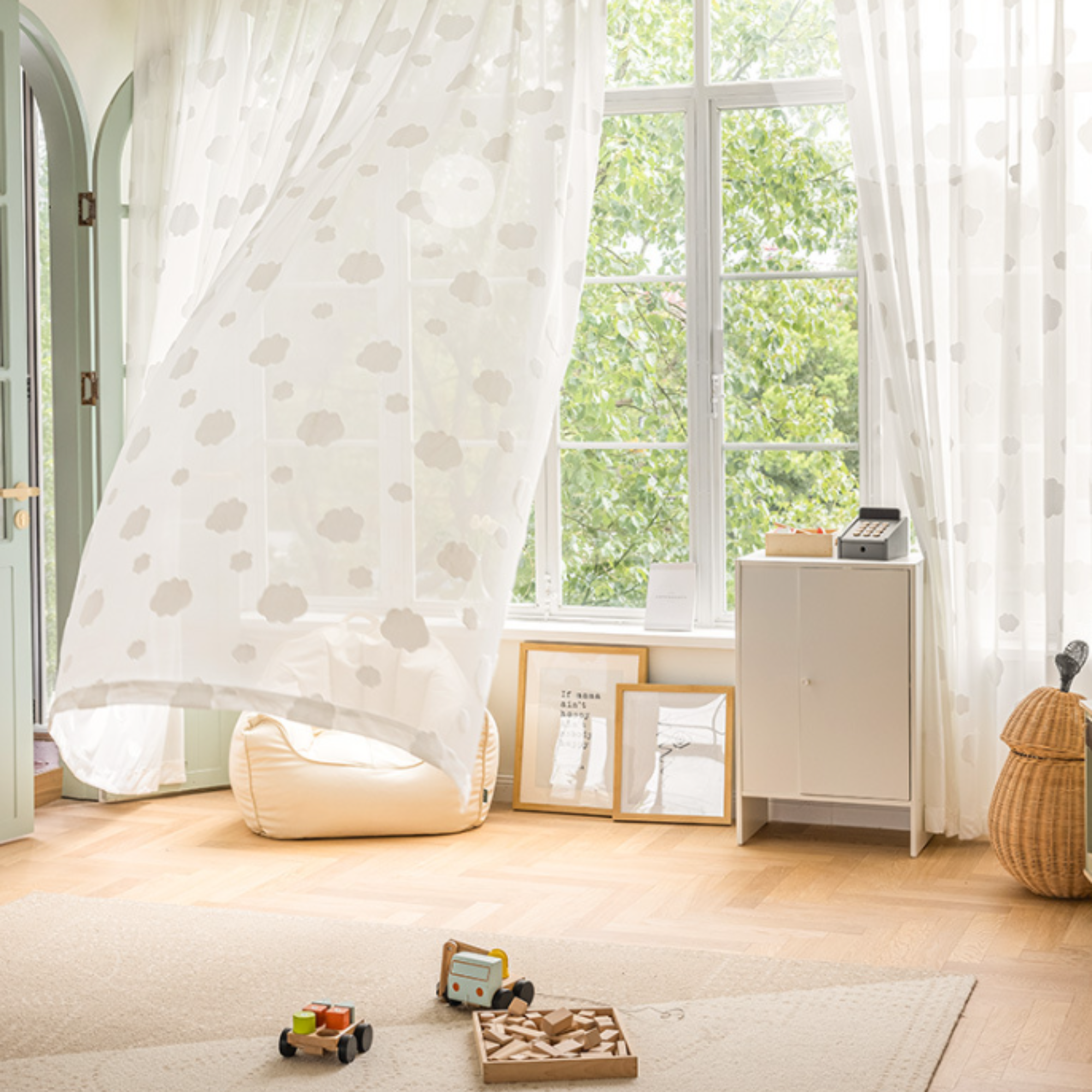 Children's playroom with toys on the floor, a white cabinet, and white cloud patterned sheer curtains.