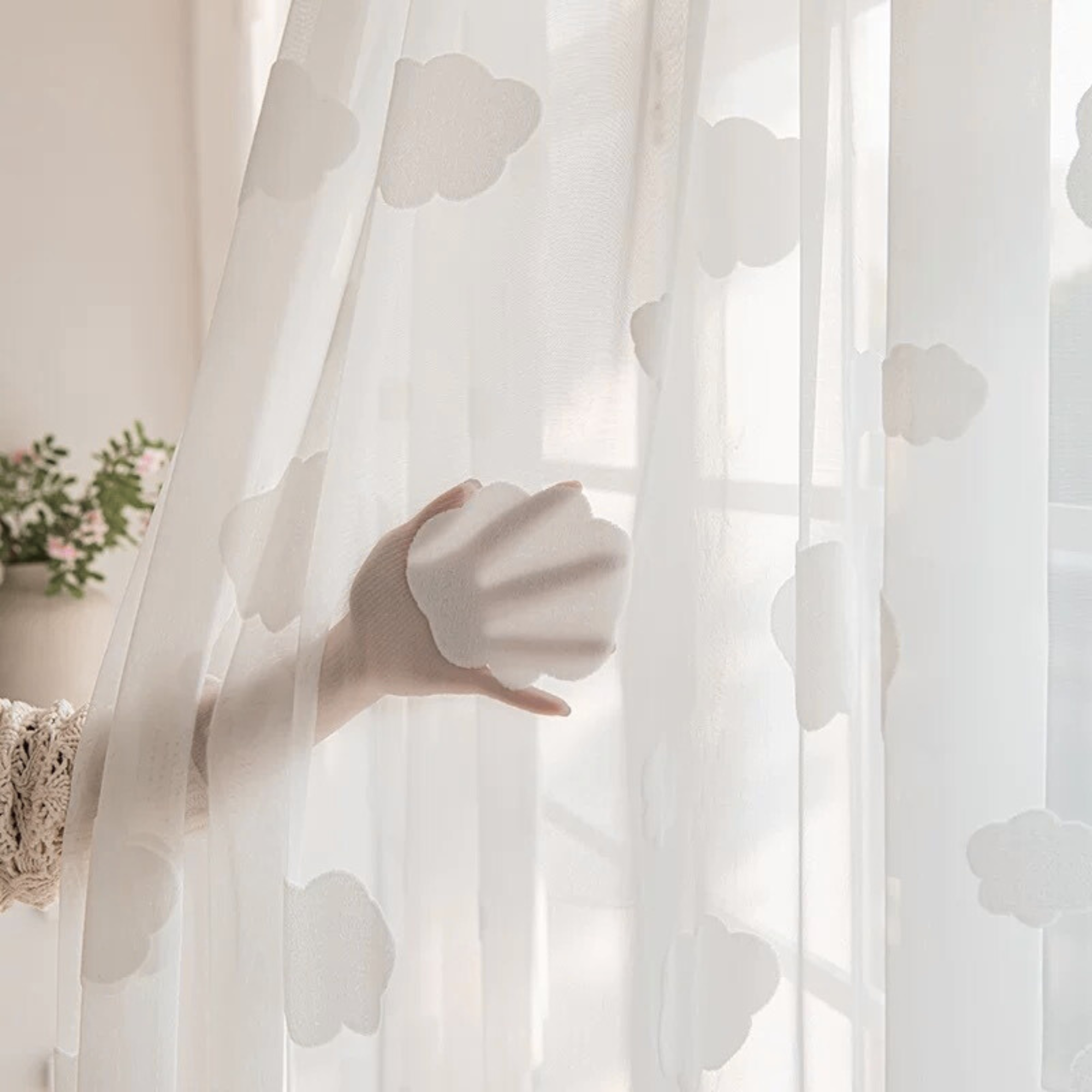 White cloud patterned sheer curtain with a hand holding it back, showing how see through the curtains are.