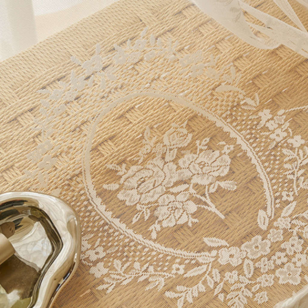A close-up an ivory embroidered floral oval design on lace drapery, shown with a small metallic bowl in the lower left corner.