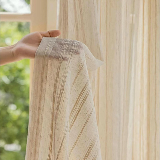 Hand holding a piece of beige linen curtain fabric with subtle stripe patterns against a blurred natural background