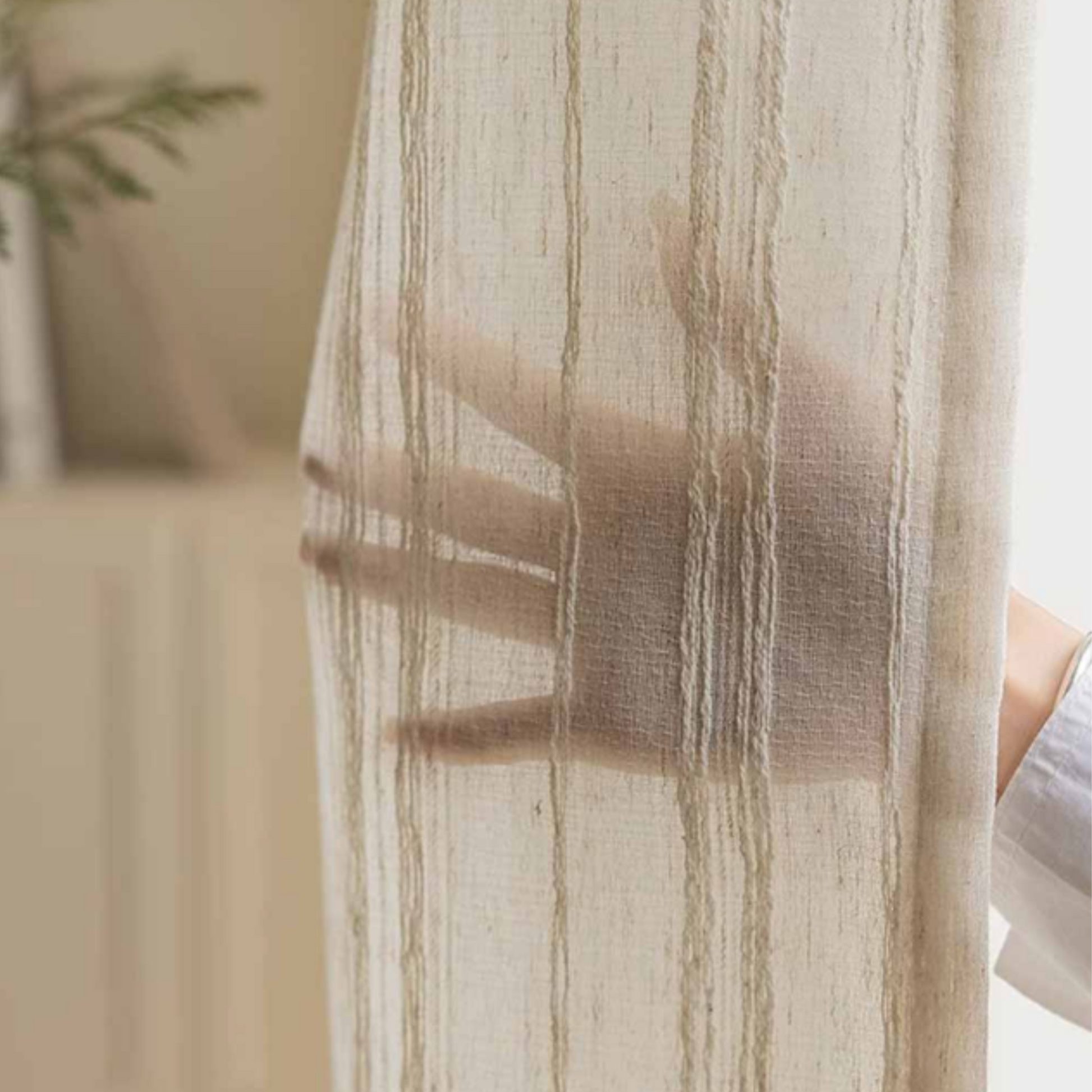 Sheer striped linen curtain with a blurred hand behind it showing how much privacy it can provide