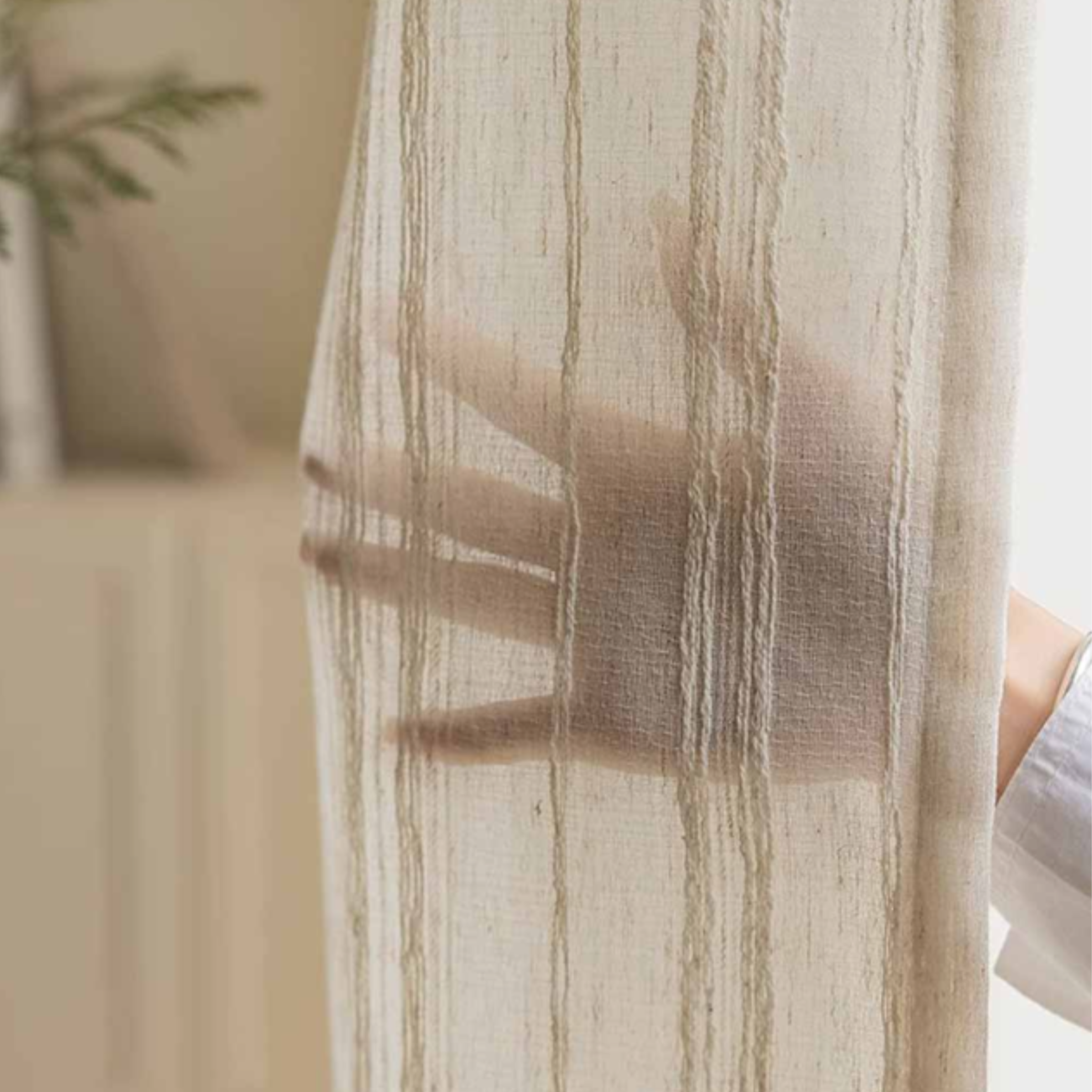 Sheer striped linen curtain with a blurred hand behind it showing how much privacy it can provide