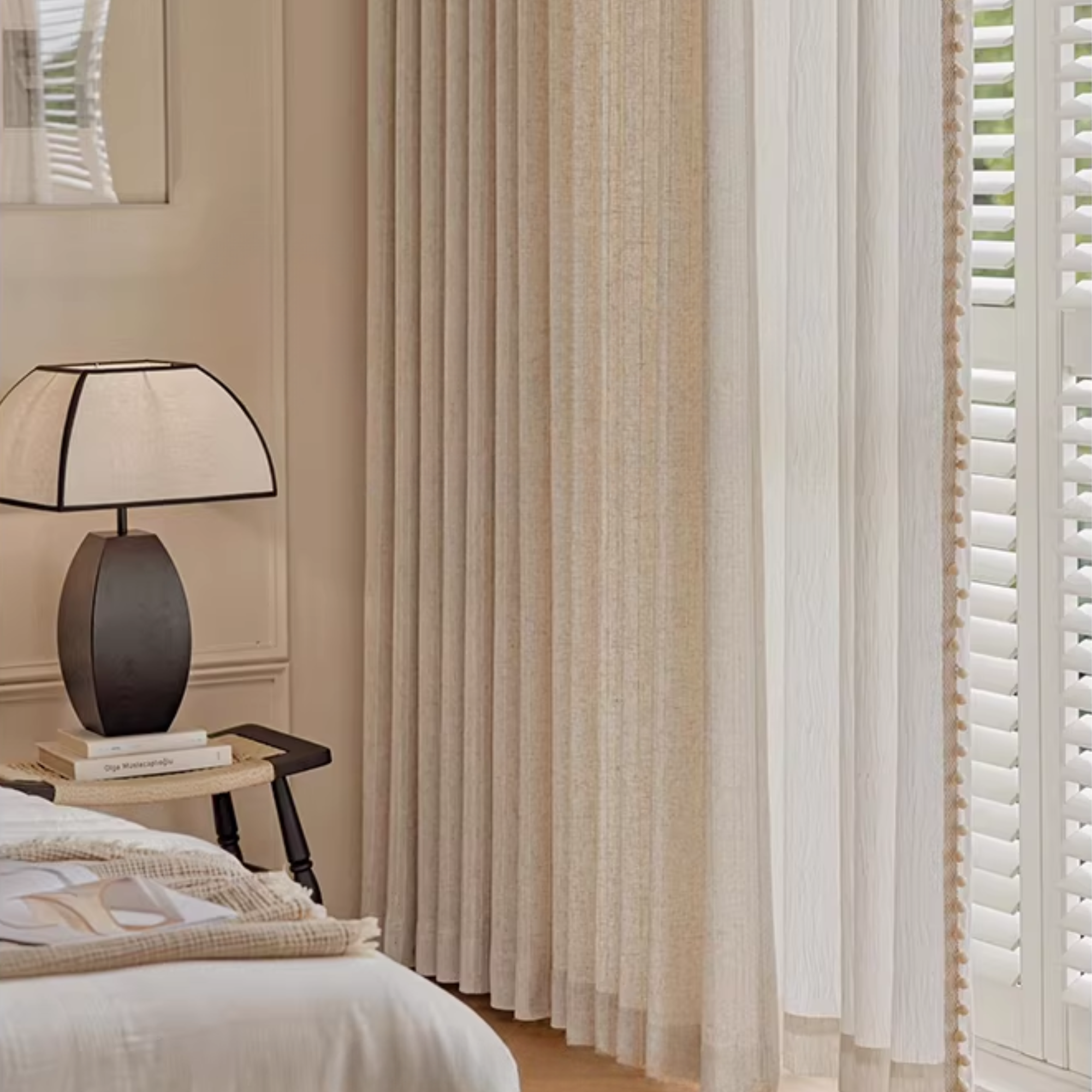 Bedroom with a lamp on a nightstand, white linen curtains, and shutters.