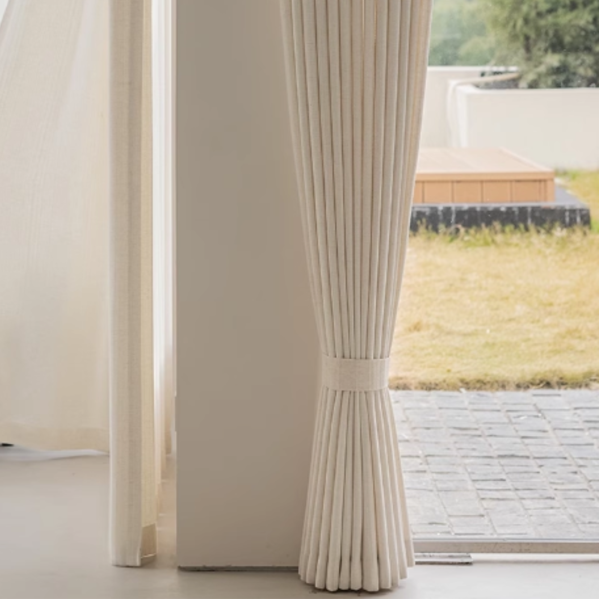Beige pleated linen curtains with a blurred outdoor scene in the background