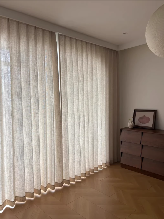Beige linen curtains in a living room with a wooden floor and a dresser.