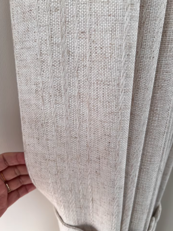 Close-up of a textured cream linen curtain with a hand holding it.